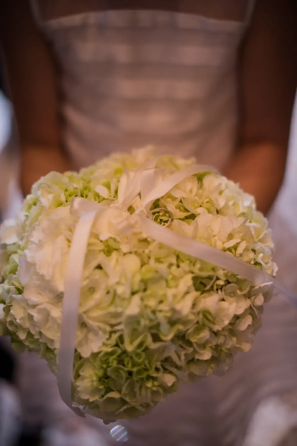 Una persona con un abito senza spalline regge un bouquet sferico di ortensie verde chiaro e bianche legate con un nastro bianco. L'attenzione è rivolta al bouquet, con l'abito leggermente sfocato sullo sfondo.