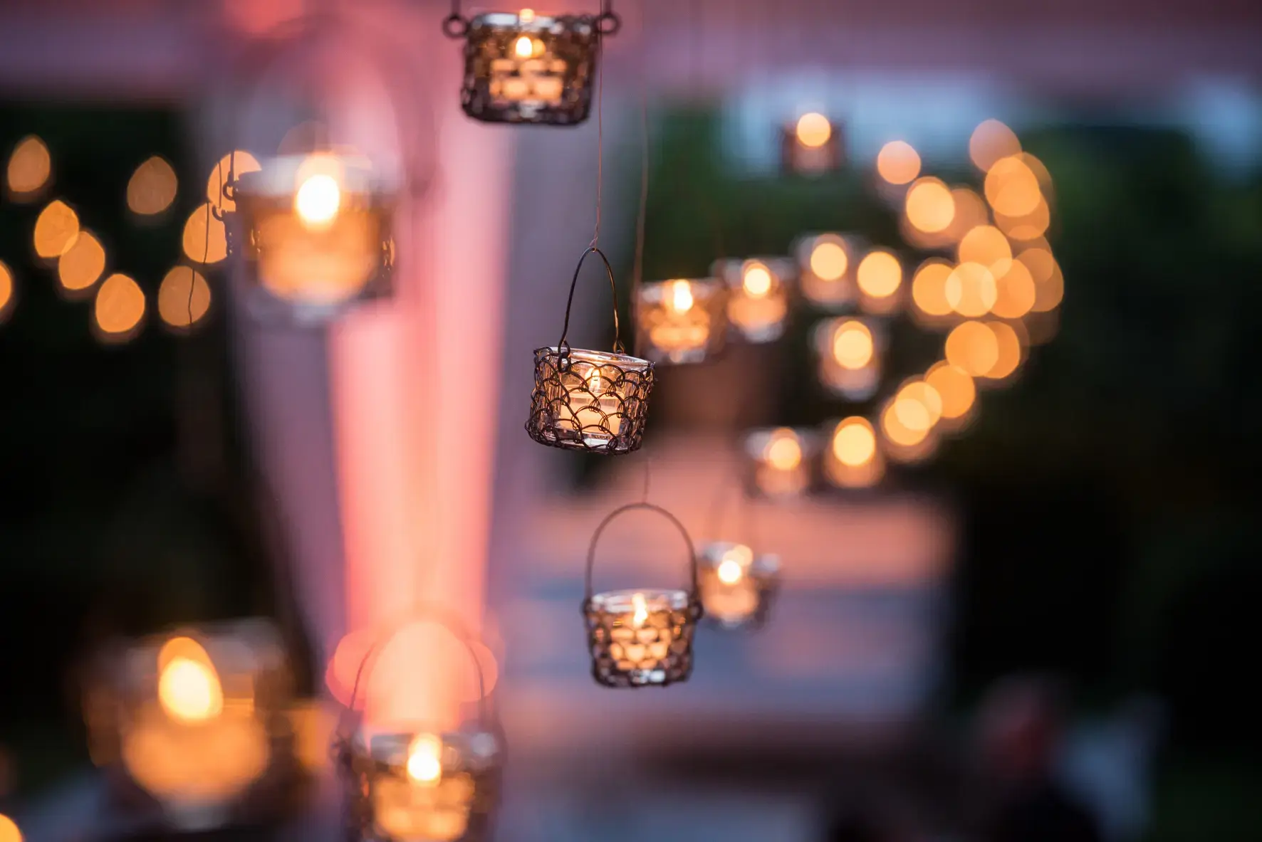 Portacandele sospesi con candele accese creano un'atmosfera calda e romantica. Sullo sfondo si vedono luci sfocate di fili di luci, che accentuano l'atmosfera accogliente.