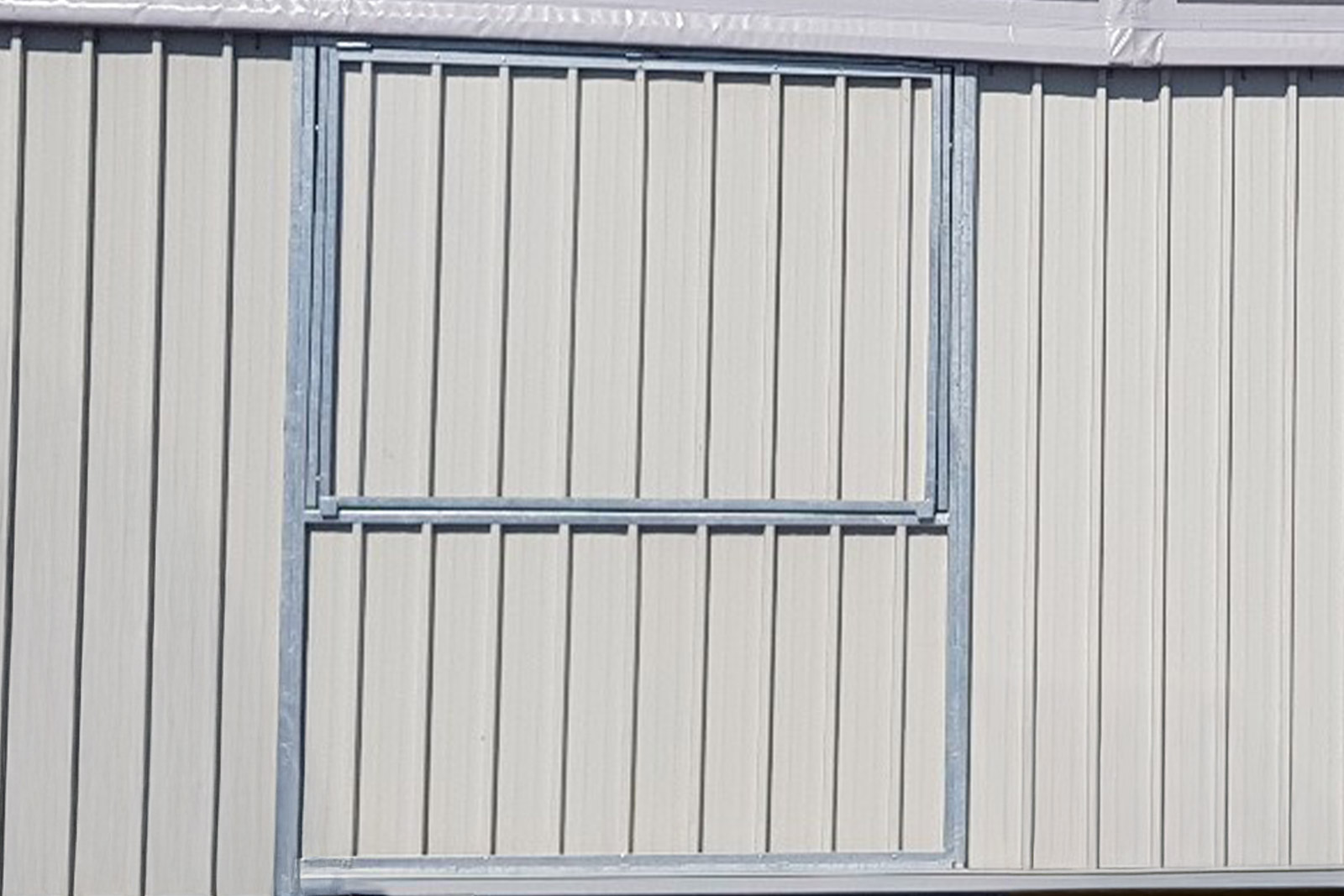 Una sezione di parete metallica grigio chiaro con pannelli verticali e una cornice rettangolare, probabilmente per una finestra o una porta, delineata da un bordo metallico.